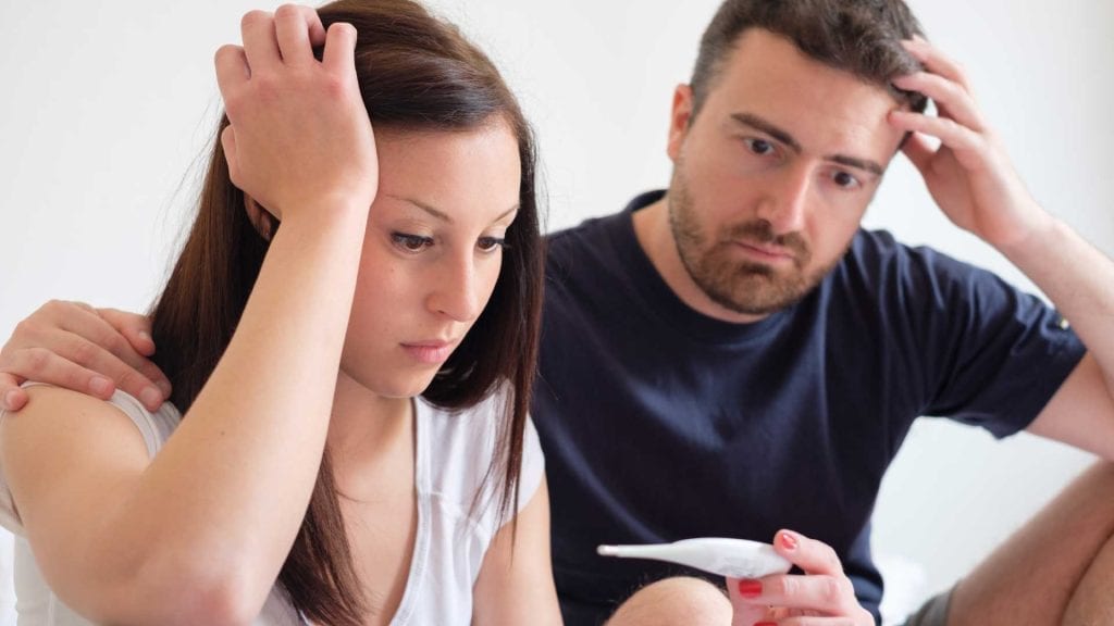 Couple looking concerned while holding a pregnancy test, representing infertility problems