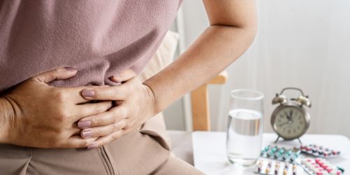 Person clutching abdomen in discomfort with medicine, water, and a clock on a bedside table, illustrating symptoms before gut health testing