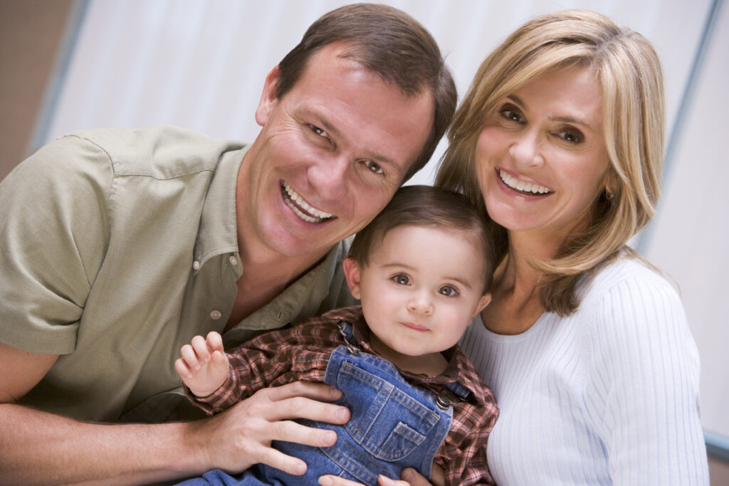 Young parents sitting close together, holding their toddler in a family portrait