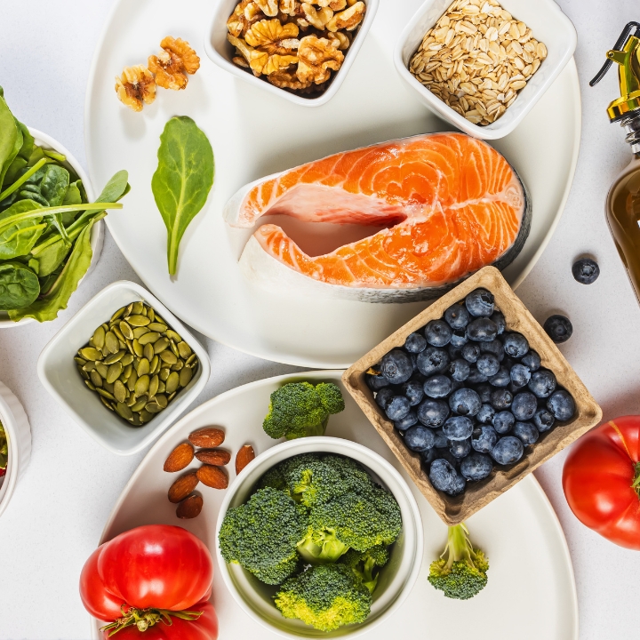 Assorted healthy foods including salmon, nuts, seeds, leafy greens, broccoli, and blueberries for nutritional health