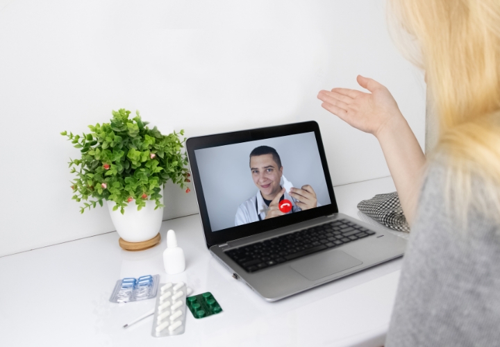 Woman consulting with a doctor online via video call on a laptop, with medications on the desk