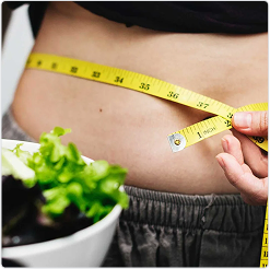 Person measuring their waist with a yellow tape measure, with a bowl of salad in the foreground, representing weight loss.