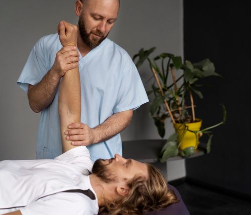 Chiropractor assists patient with arm and shoulder mobility exercise during chiropractic care session