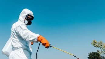 Person in a protective suit and respirator spraying chemicals outdoors, representing precautions against heavy metal toxicity